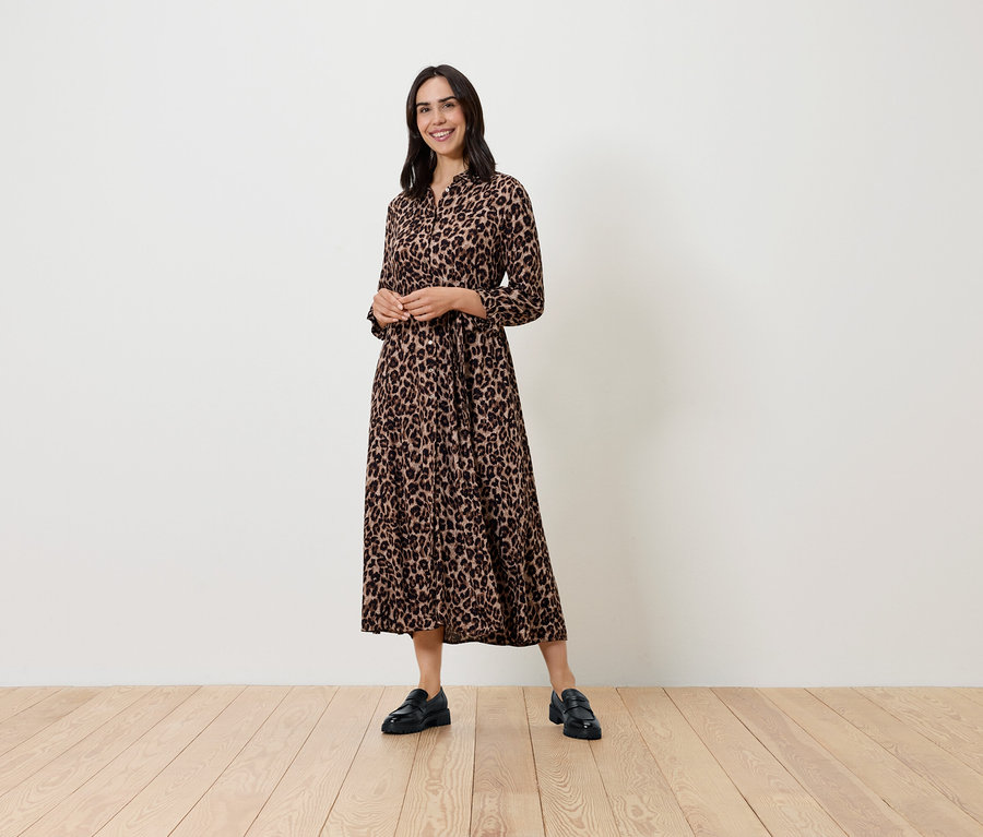 Žena pózuje ve vzorovaných šatech s dlouhým rukávem a černých botách.