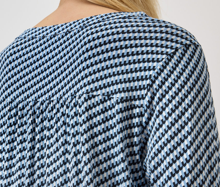 Pohled zezadu na ženu s blond vlasy v modrobílé haleně se vzorem kohoutí stopy.