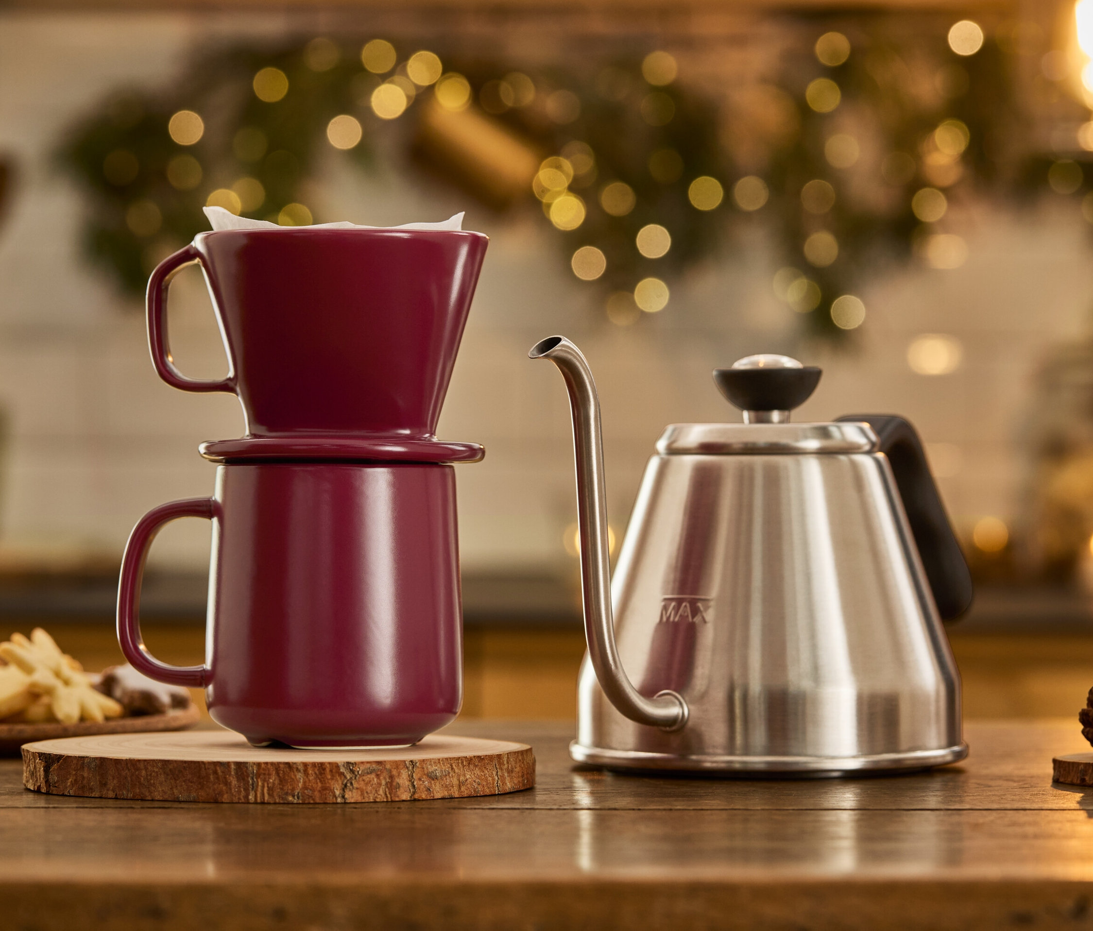Nerezová konvice s labutí hubicí stojí vedle sebe s vínovým hrnkem na kávu s filtrem, který stojí na dřevěném podstavci.