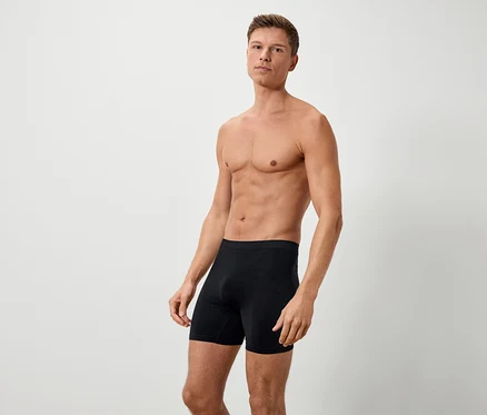 Muž s odhaleným vrškem těla stojí na bílém pozadí v černých boxerkách.