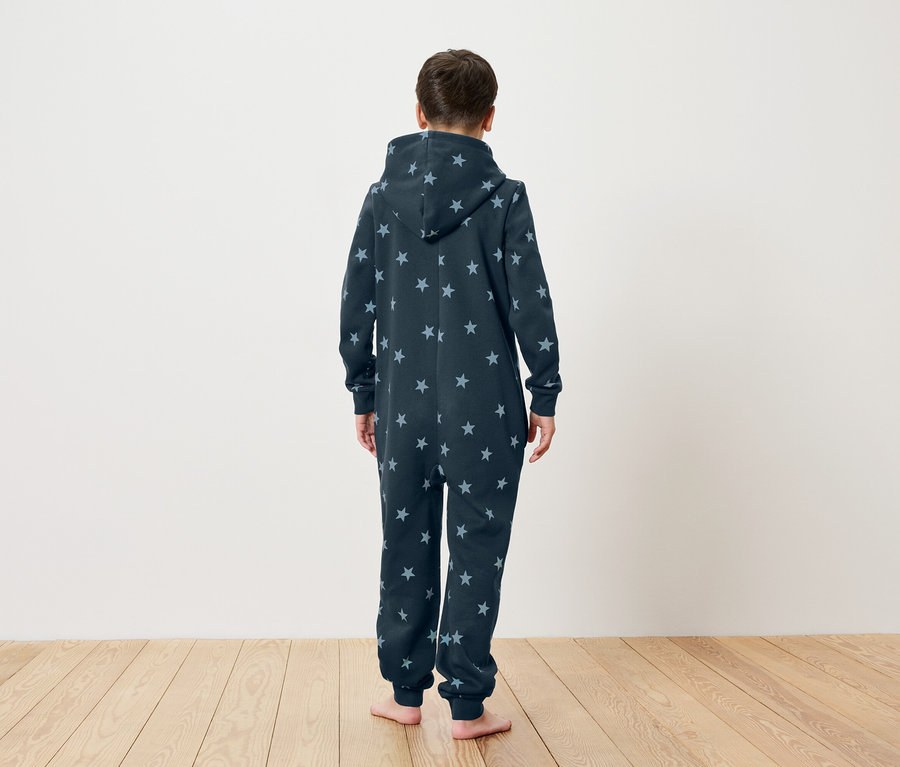 Dítě stojí zády ke kameře a má na sobě tmavě modrou kombinézu s hvězdami a kapucí.