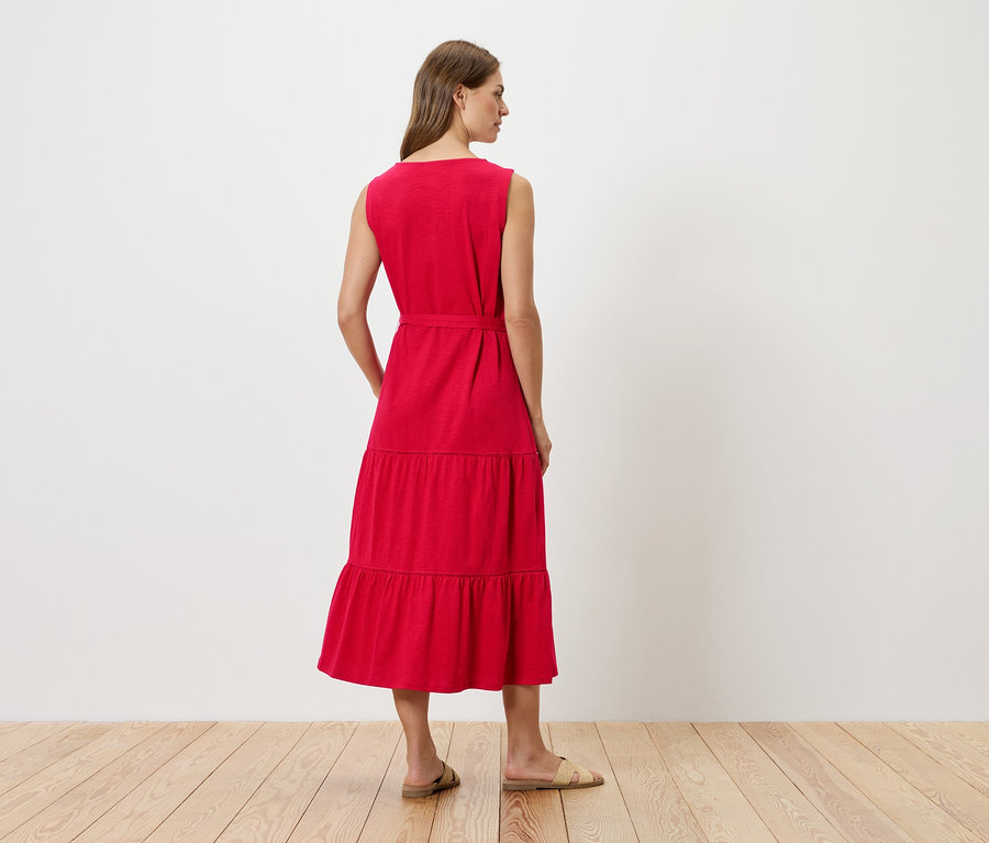 Žena zezadu v červených midi šatech bez rukávů s páskem a plochými sandály.