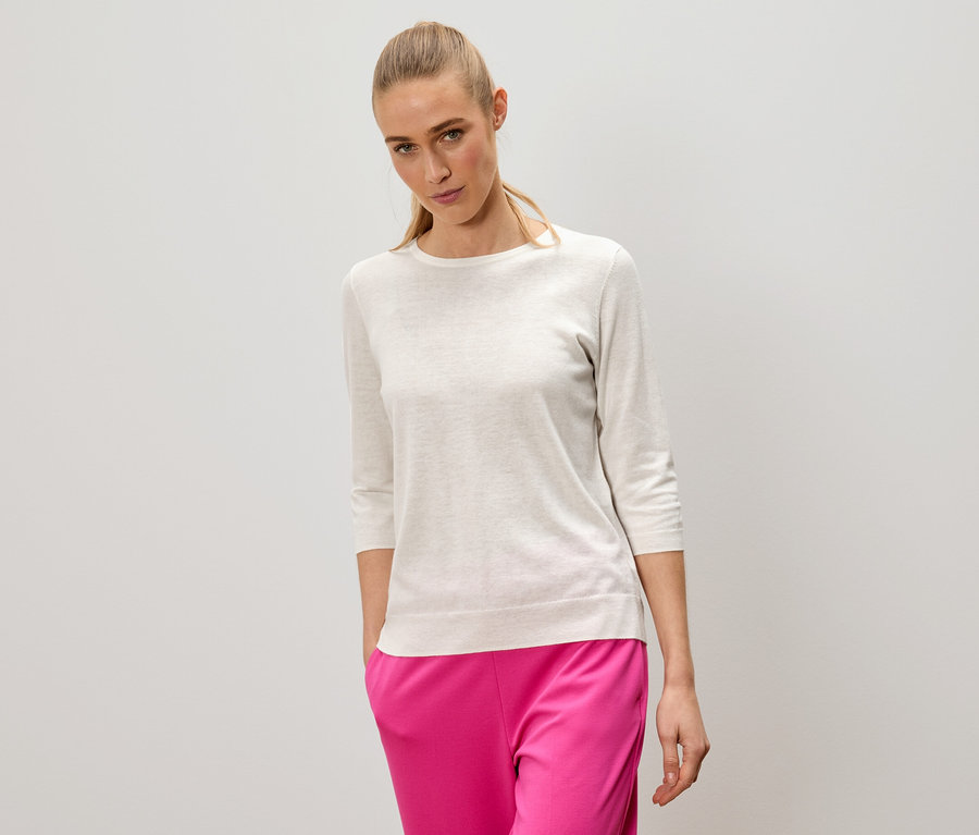 Žena s blond vlasy má na sobě světlý svetr a růžové kalhoty.