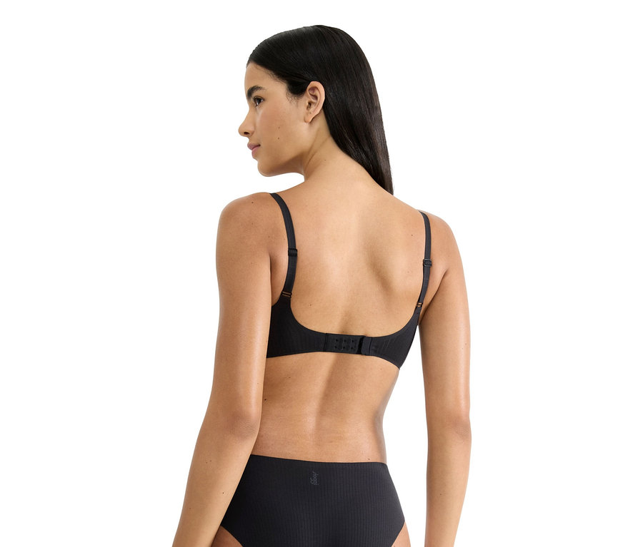 Pohled zezadu na ženu s dlouhými tmavými vlasy, která má na sobě černou podprsenku a spodní prádlo.