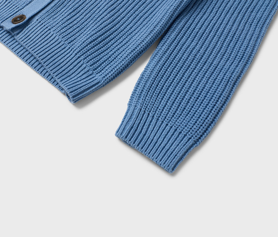 Detailní pohled na světle modrý pletený svetr s hnědými knoflíky.
