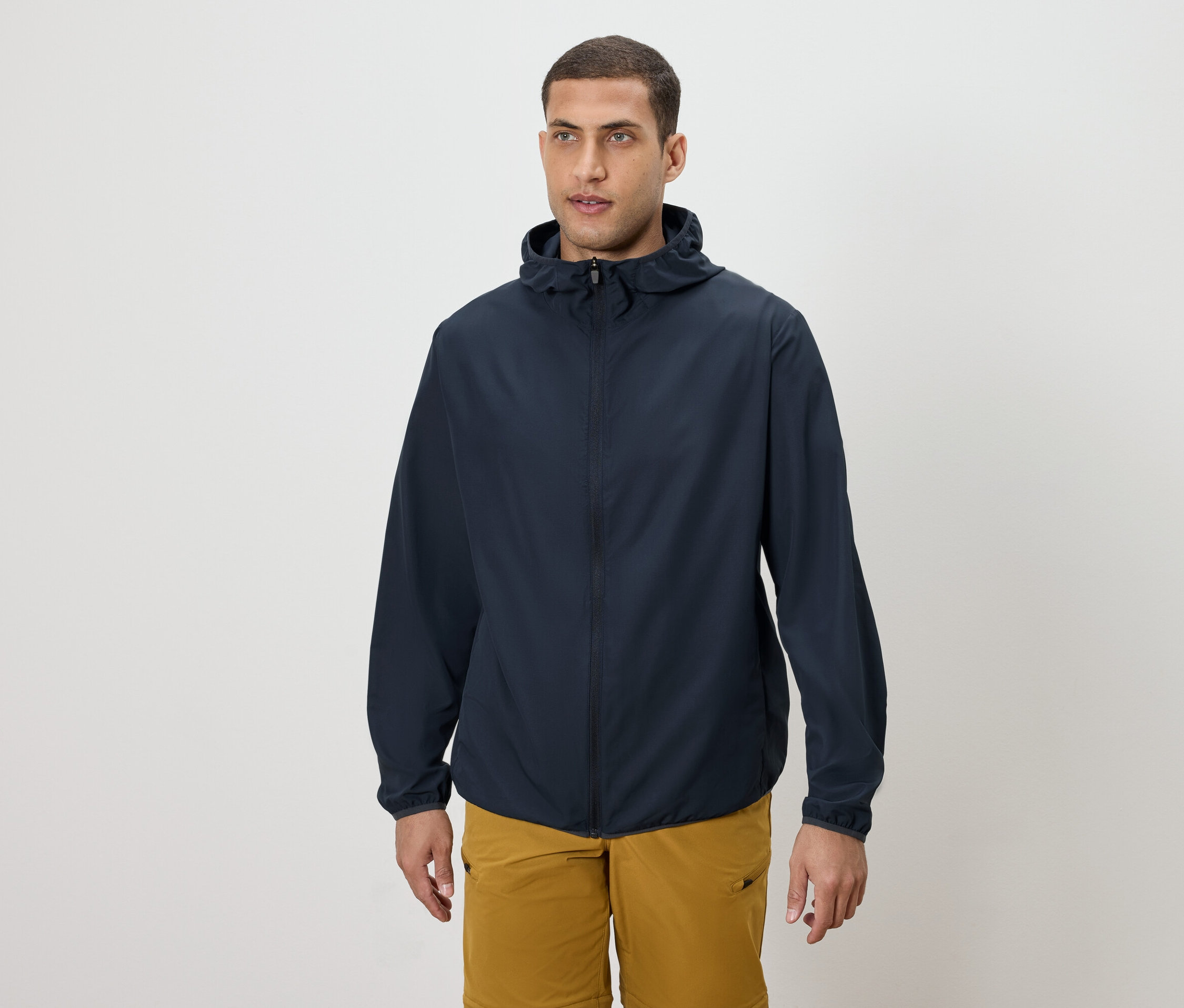 Muž má na sobě tmavě modrou bundu s kapucí a zlaté šortky.