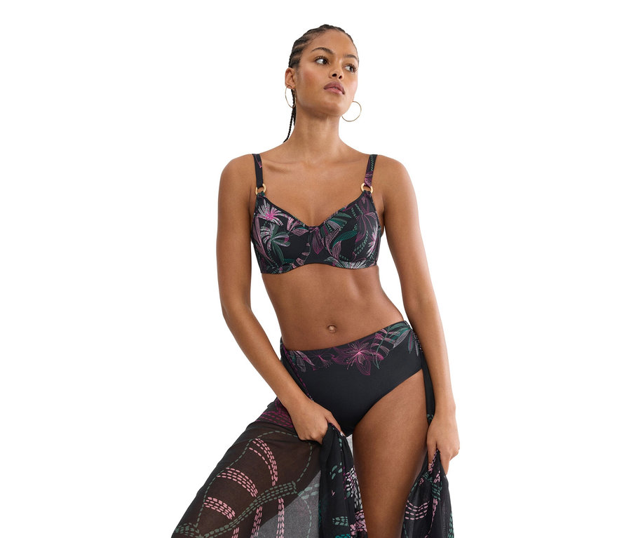 Žena má na sobě černé bikiny s květinovým vzorem a drží odpovídající pareo.