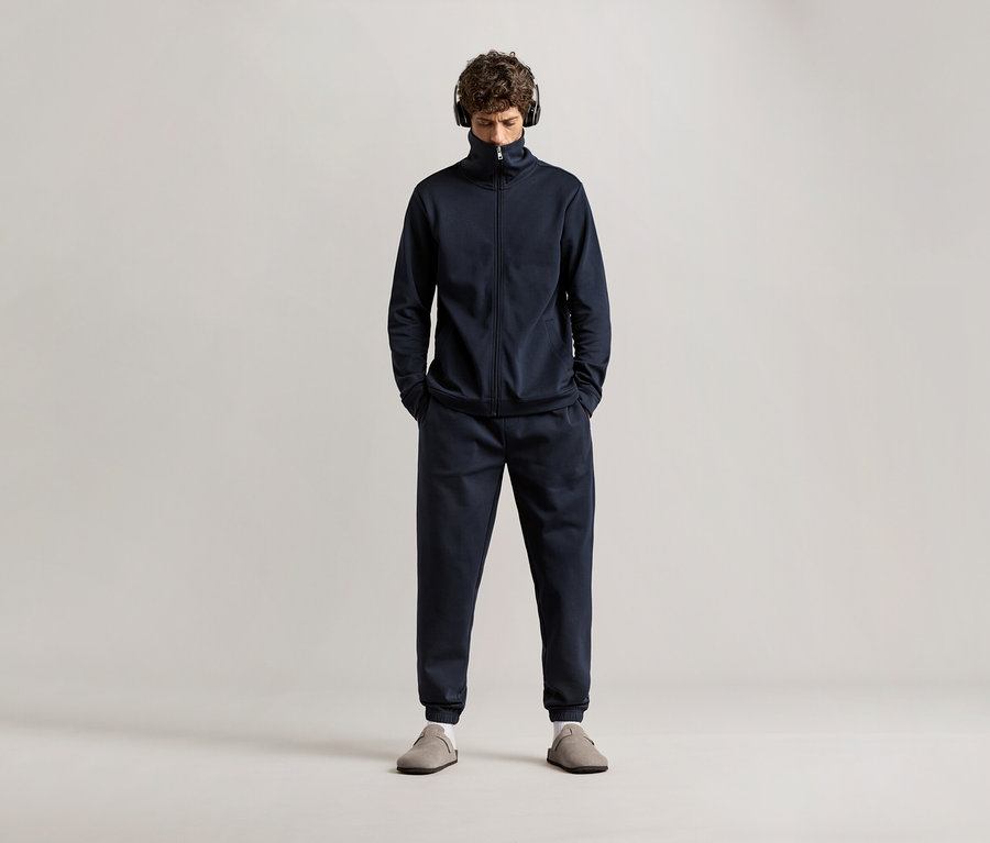 Muž se sluchátky na uších v tmavě modré domácí soupravě.