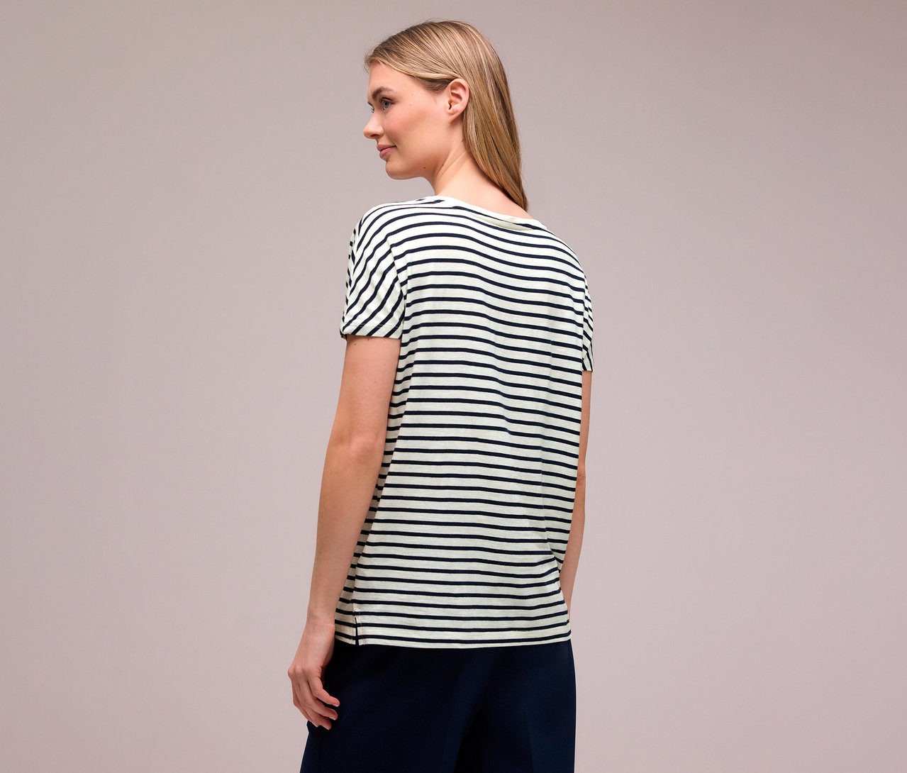 Žena zezadu s blond vlasy má na sobě námořnickou modro-bílé tričko Street One s vodorovnými pruhy.