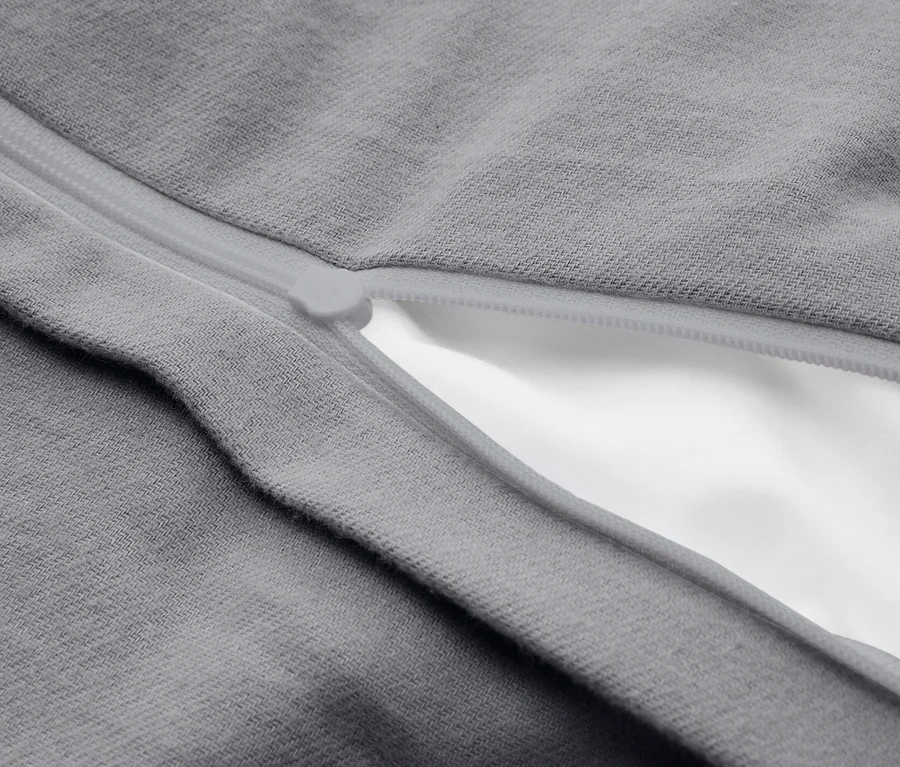 Detail šedé látky s částečně rozepnutým světle šedým zipem, který odhaluje bílou látku pod ním.
