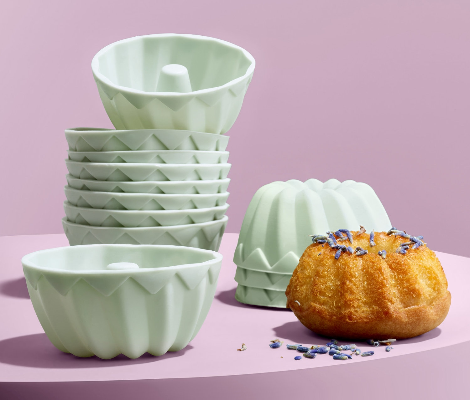 Na fialovém pozadí jsou formičky na minibábovky, 12 ks, jedna bábovka je posypaná levandulí.