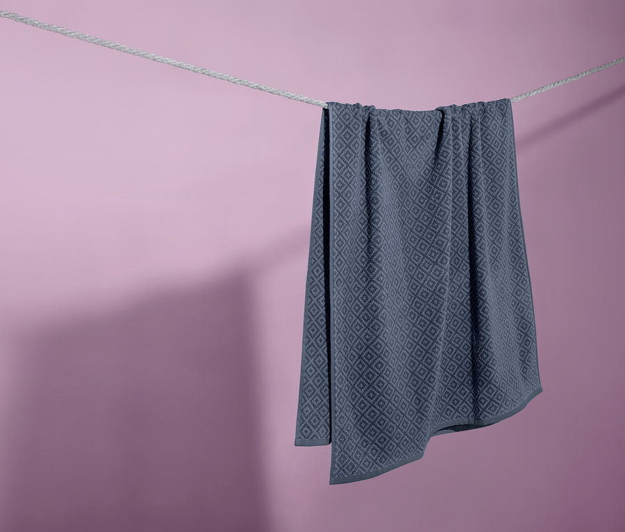 Modrá žakárová osuška visí na šňůře na prádlo před fialovým pozadím.