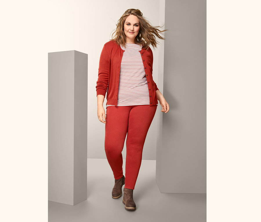 Žena kráčí a má na sobě proužkované triko s polodlouhým rukávem, džegíny, kabátek z jemné pleteniny a hnědé boty.