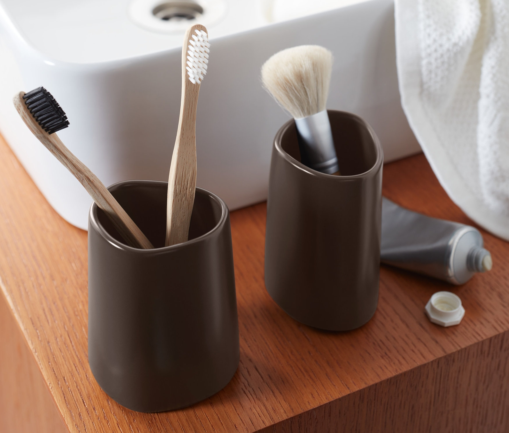 Dva hnědé kelímky na zubní kartáčky s kartáčky a štětcem na dřevěné polici.