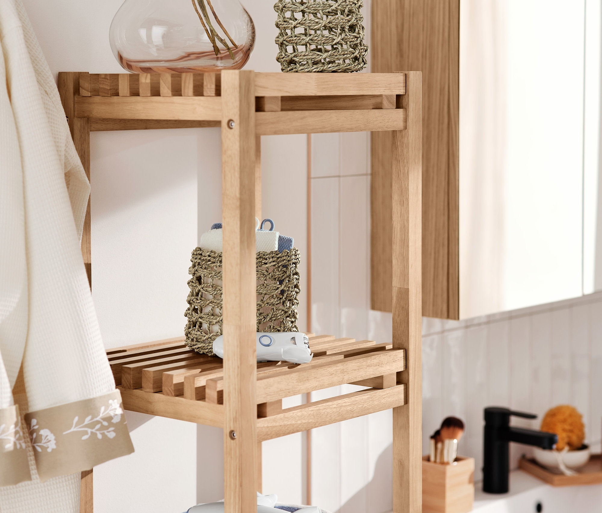 Úzký regál s košíky, osuškou, epilátorem na obličej a cestovní sadou fénu a žehličy na vlasy.