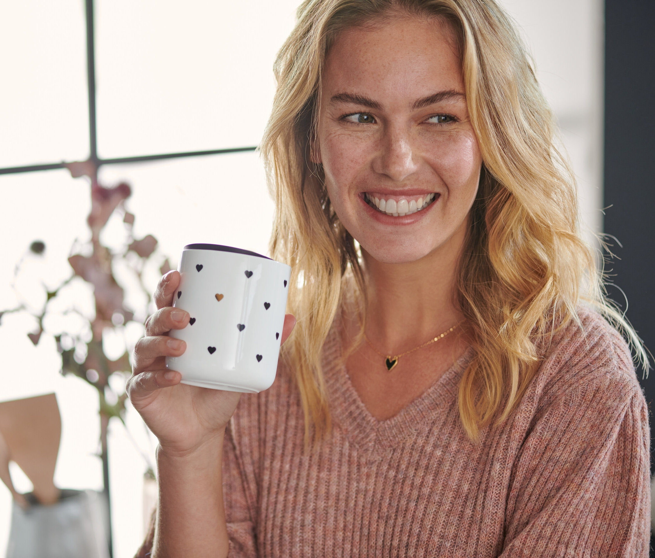 Žena drží porcelánový hrnek s víčkem a motivem srdíček.