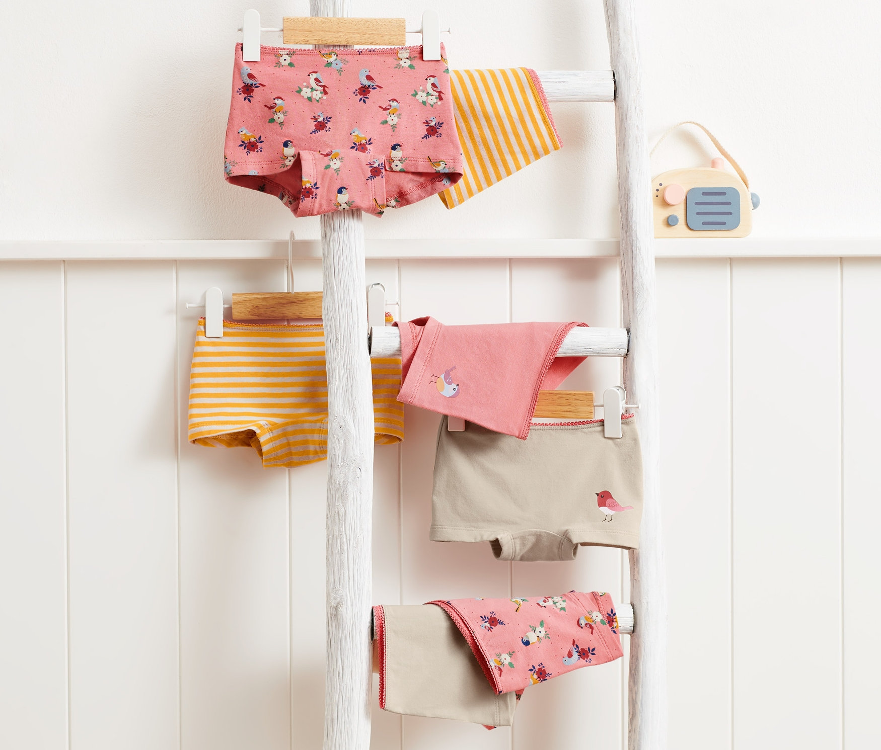 Sedmery dívčí kalhotky visí na bílém dřevěném žebříku.