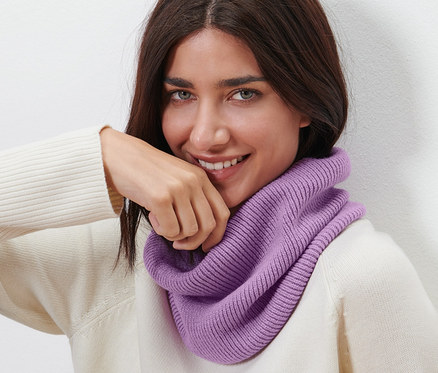 Žena s hnědými vlasy se usmívá a má na sobě pletenou kruhovou šálu.