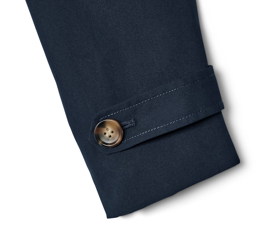 Detail rukávu tmavě modrého trenčkotu s hnědým knoflíkem.