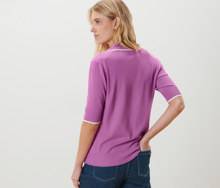 Žena pózuje v džínových kalhotách a fialové polokošili z jemného úpletu.