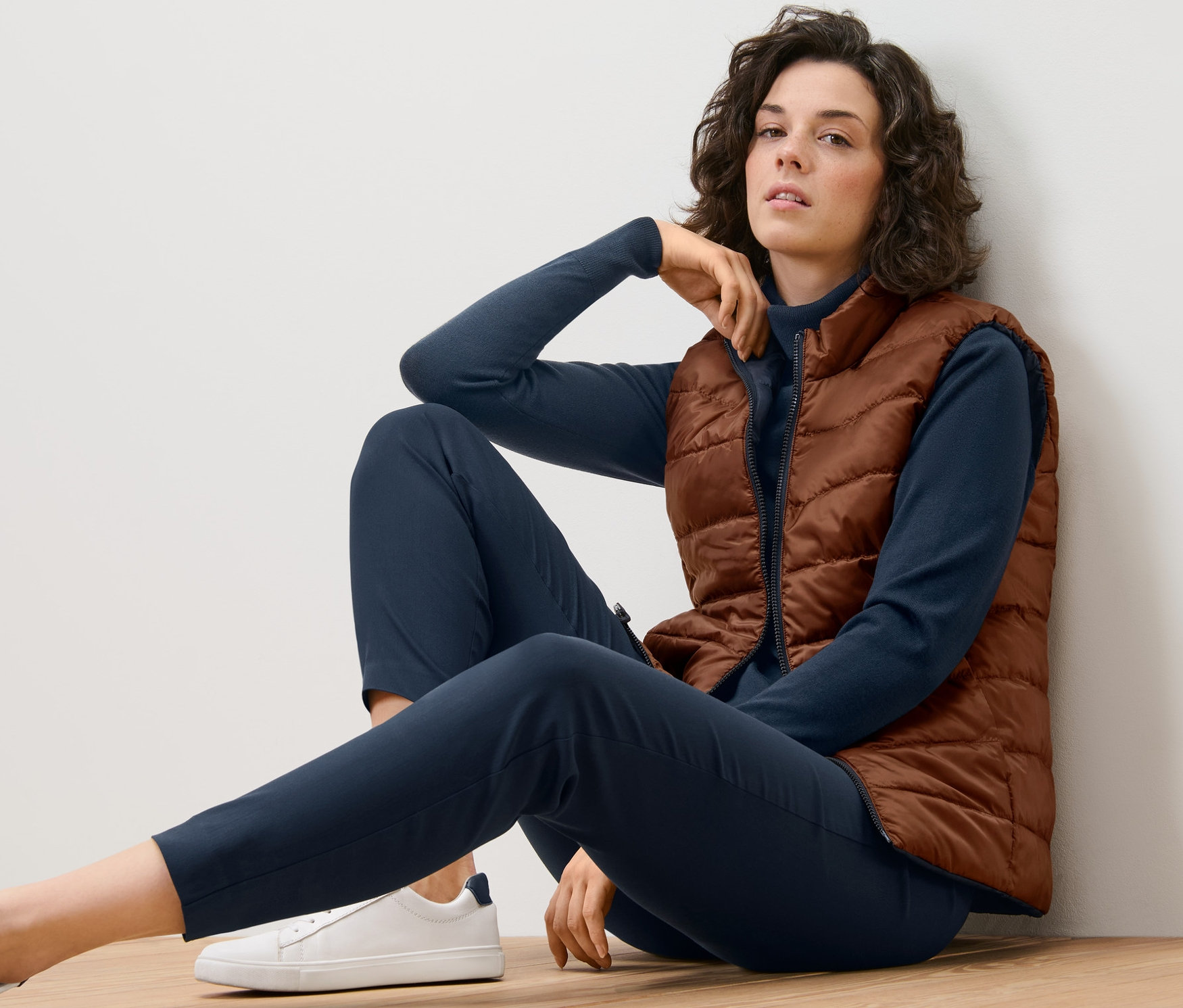 Žena sedí na podlaze a má na sobě oboustrannou prošívanou vestu.