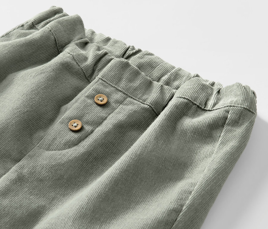 Detail dětských manšestrových navlékacích kalhot s elastickým pasem a dvěma knoflíky.