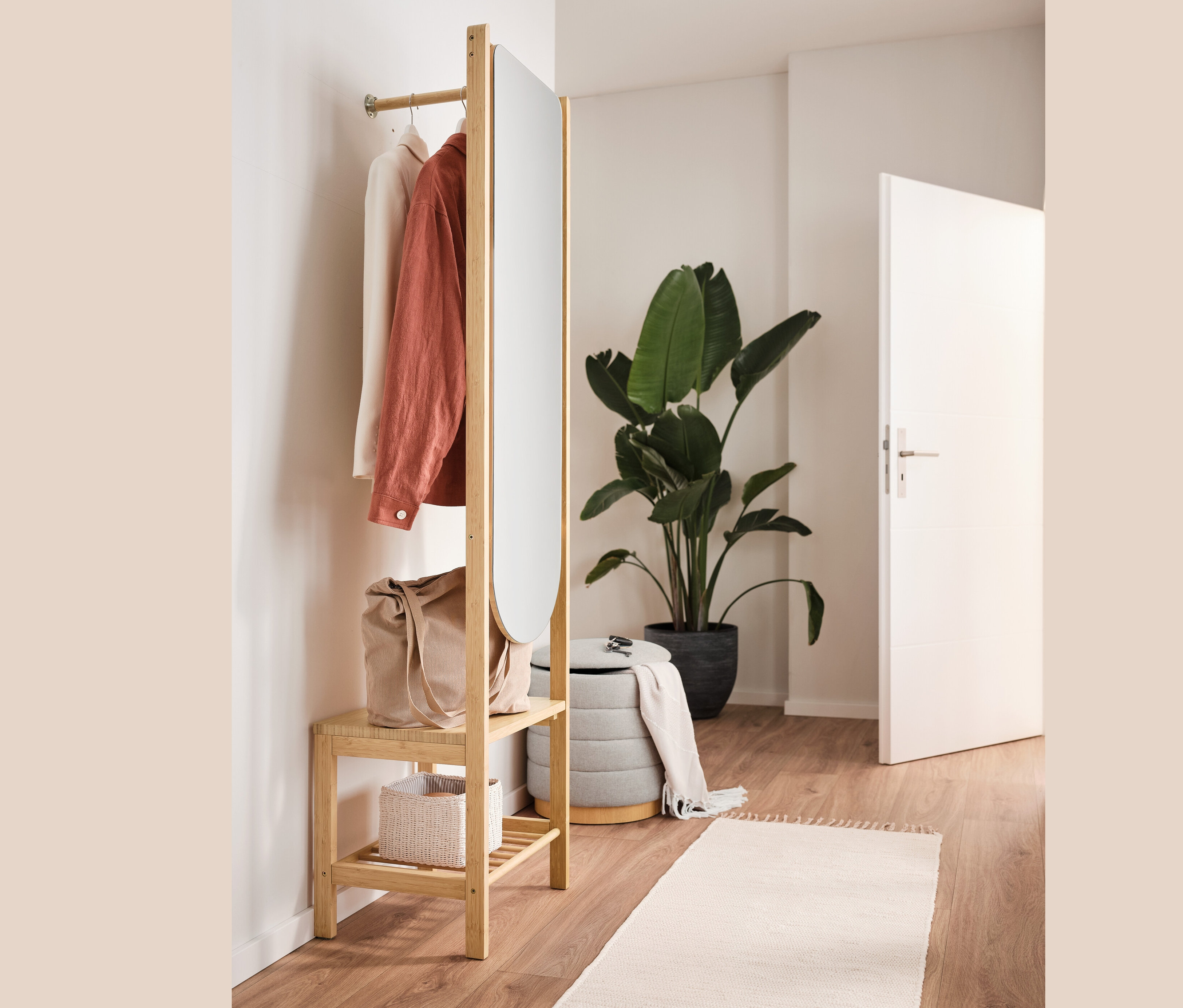 Otevřená šatní skříň se zrcadlem a odkládací plochou, puf s úložným prostorem, taška a oblečení v interiéru.