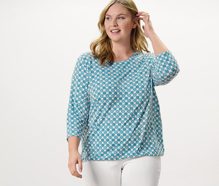 Žena stojící a pózuje v halenovém triku s celoplošným potiskem a 7/8 strečových kalhotách, bílá.