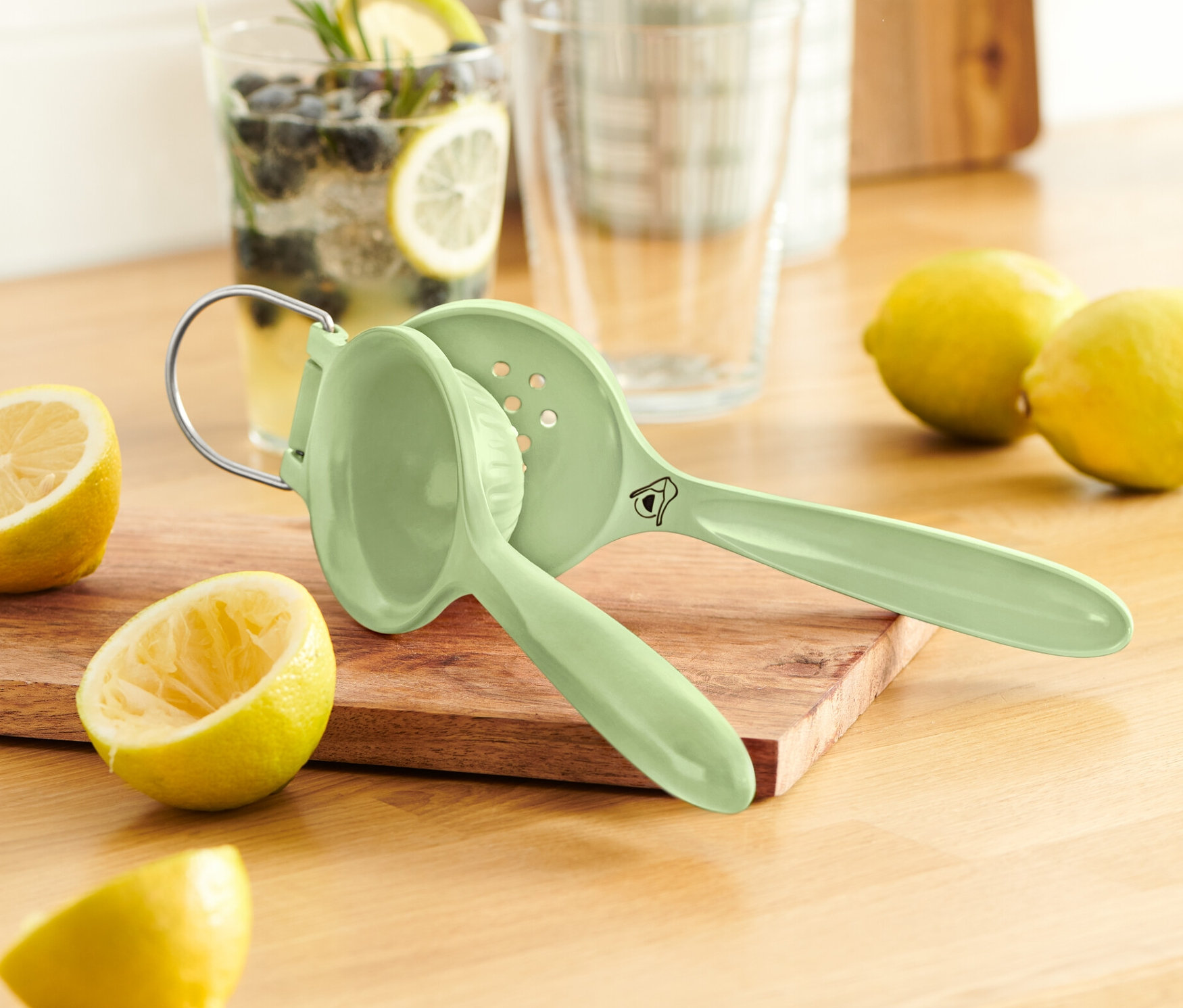 Zelený lis na citrusy na dřevěném prkénku vedle citronů.