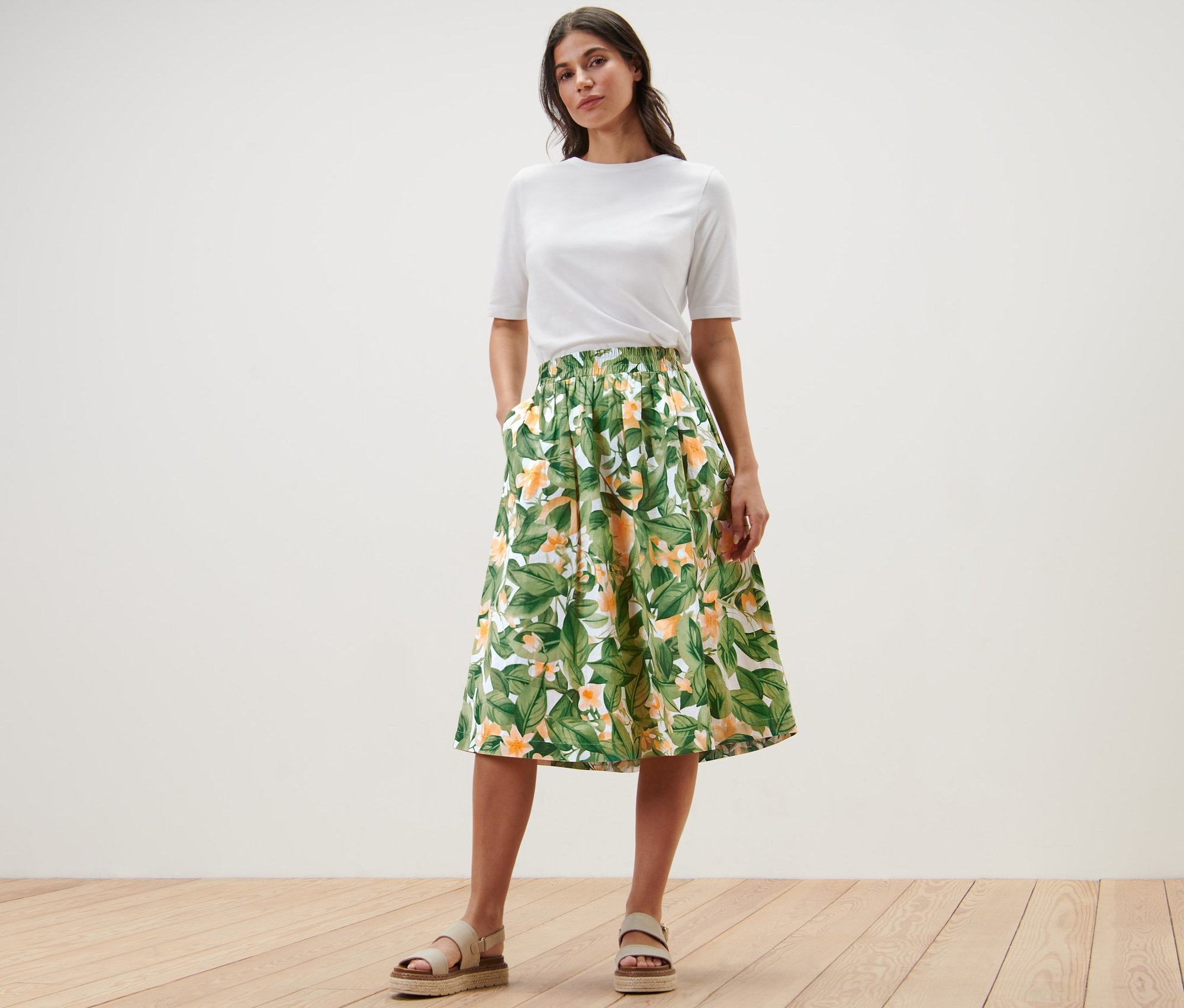 Žena pózuje v bílém tričku a popelínové sukni s potiskem.