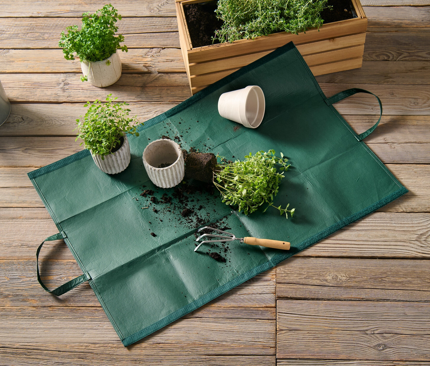 Zahradní taška na odpad leží na dřevěné podlaze vedle hrnkových rostlin a konve.