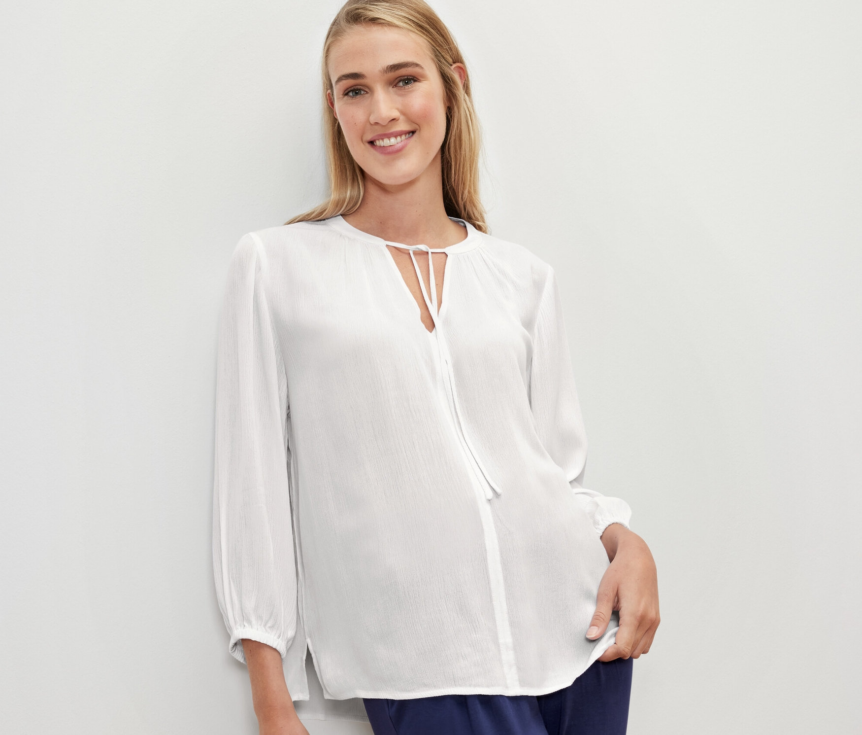 Žena má na sobě bílou tunikovou halenku.