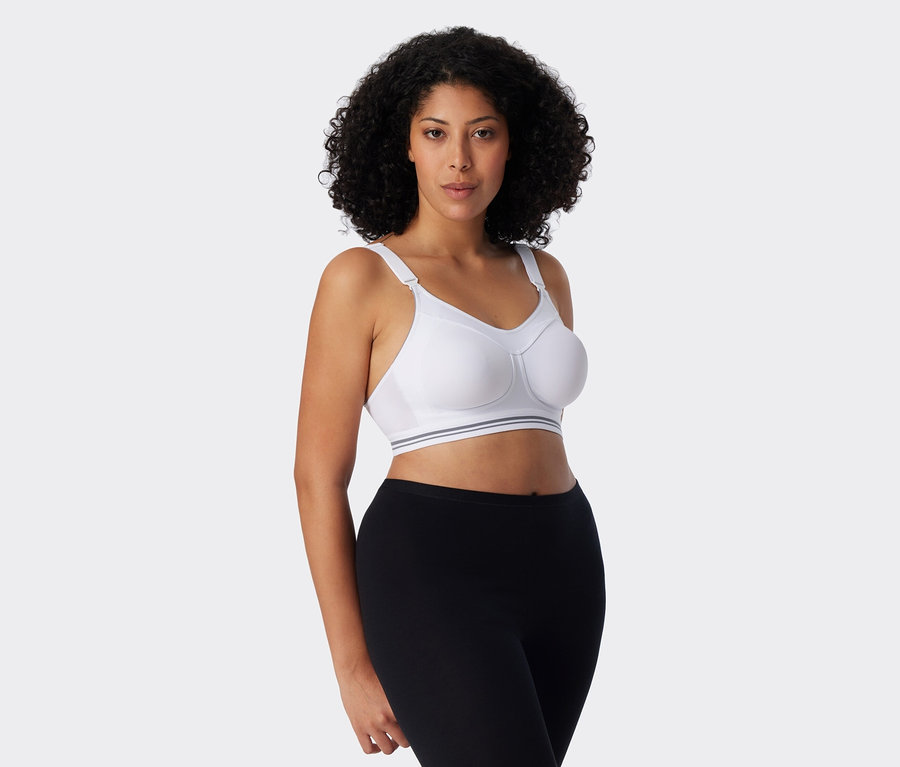 Žena s kudrnatými vlasy má na sobě bílou sportovní podprsenku a černé legíny.
