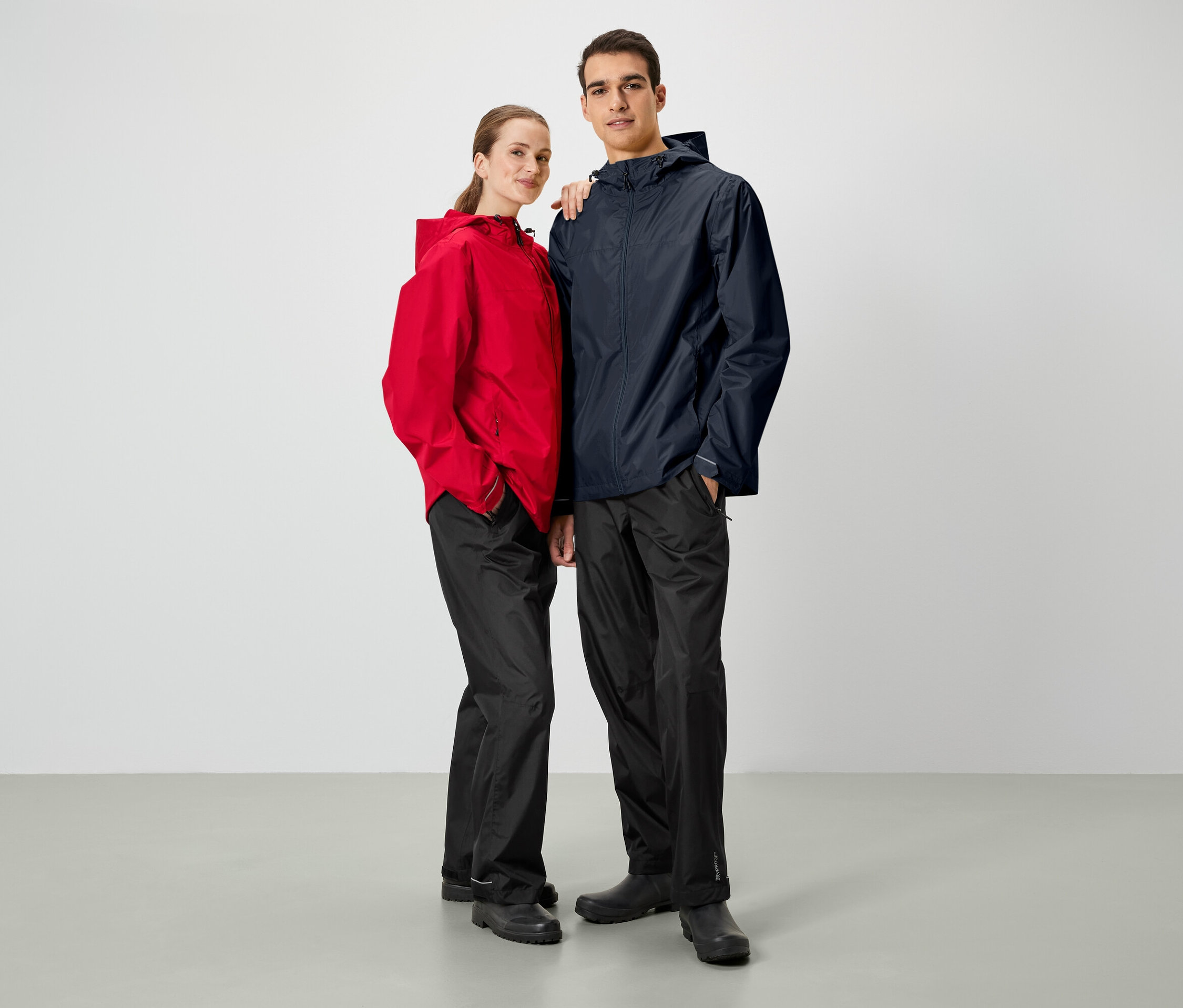 Muž a žena pózují vedle sebe. Oba nosí bundy do deště a černé kalhoty.