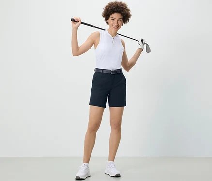 Žena drží golfovou hůl za rameny a má na sobě tmavě modré softshellové funkční šortky.