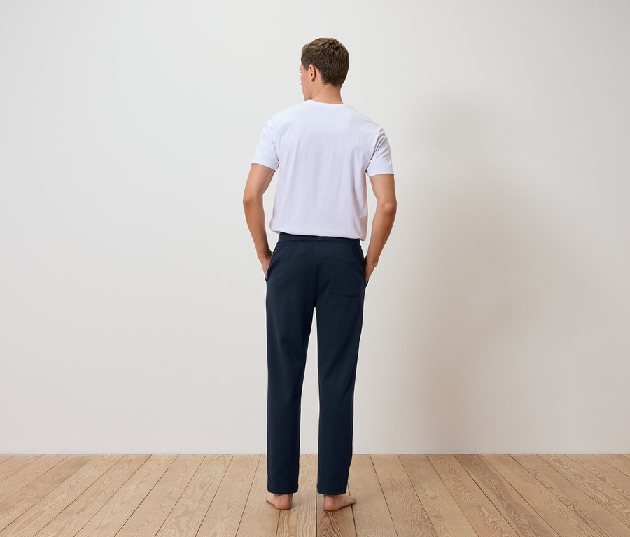 Muž zády k fotoaparátu má na sobě bílé tričko a tmavě modré kalhoty.