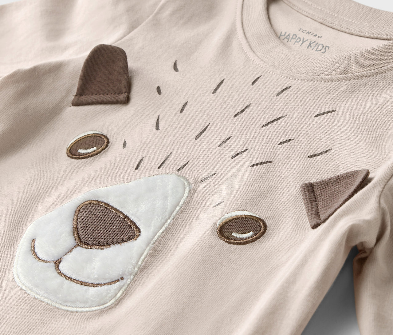 Detail dětského trička s dlouhým rukávem s motivem obličeje medvěda a lesních zvířat.