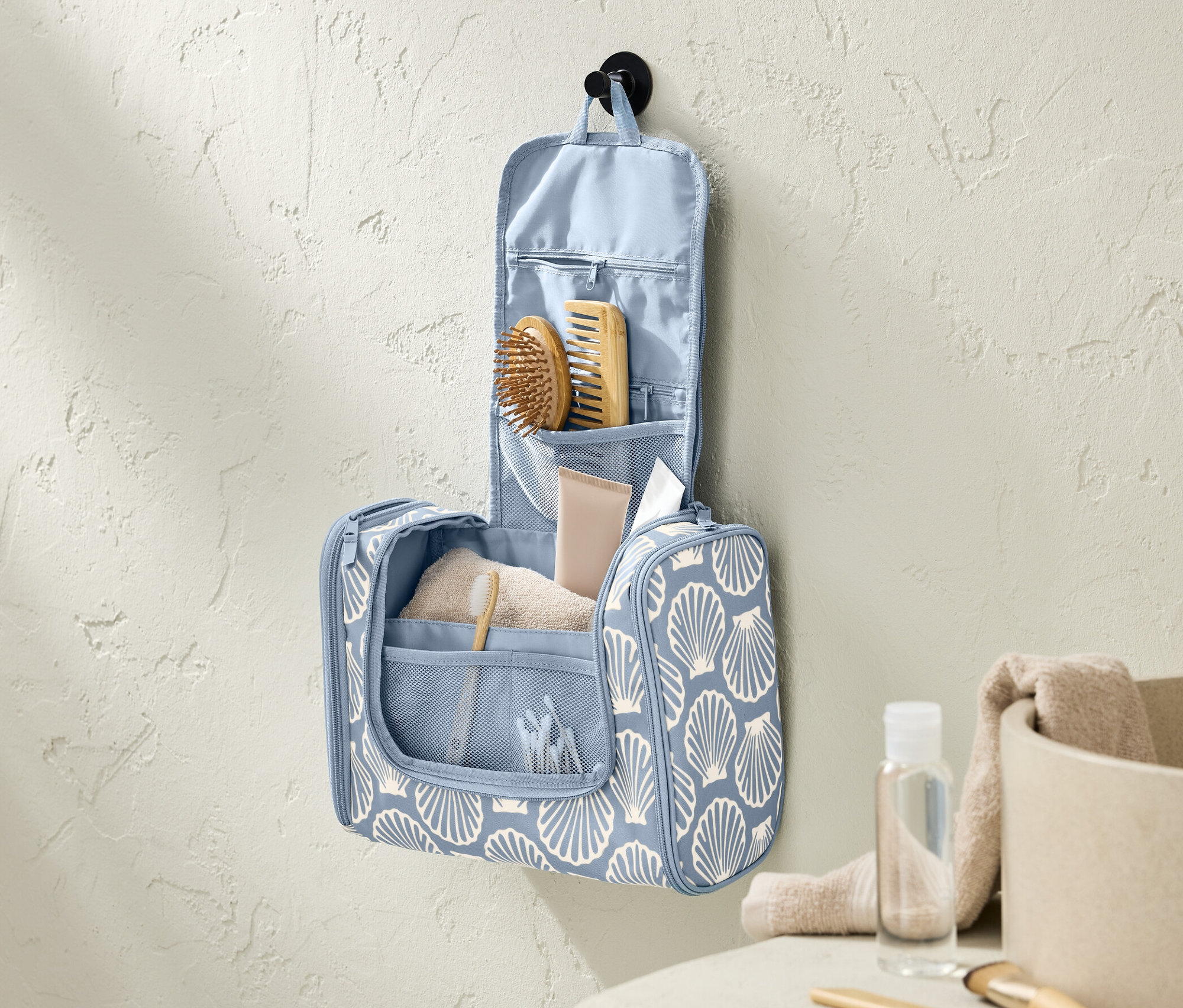 Modrá toaletní taštička s potiskem mušlí visí na zdi v koupelně.
