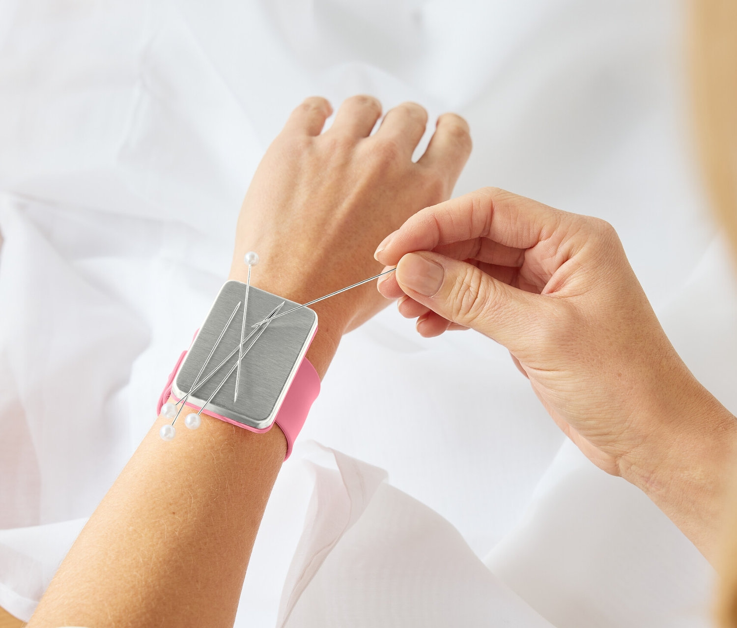 Žena šije látku a má na zápěstí magnetický držák jehel Armnadelkissen.