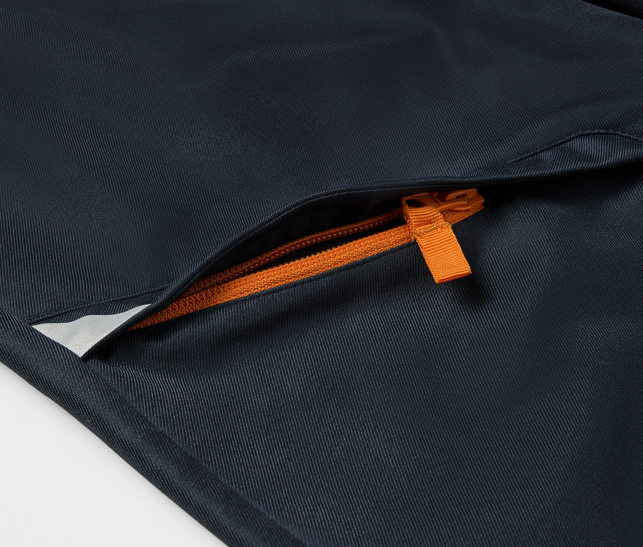 Detail dětských softshellových kalhot s oranžovým zipem kapsy.