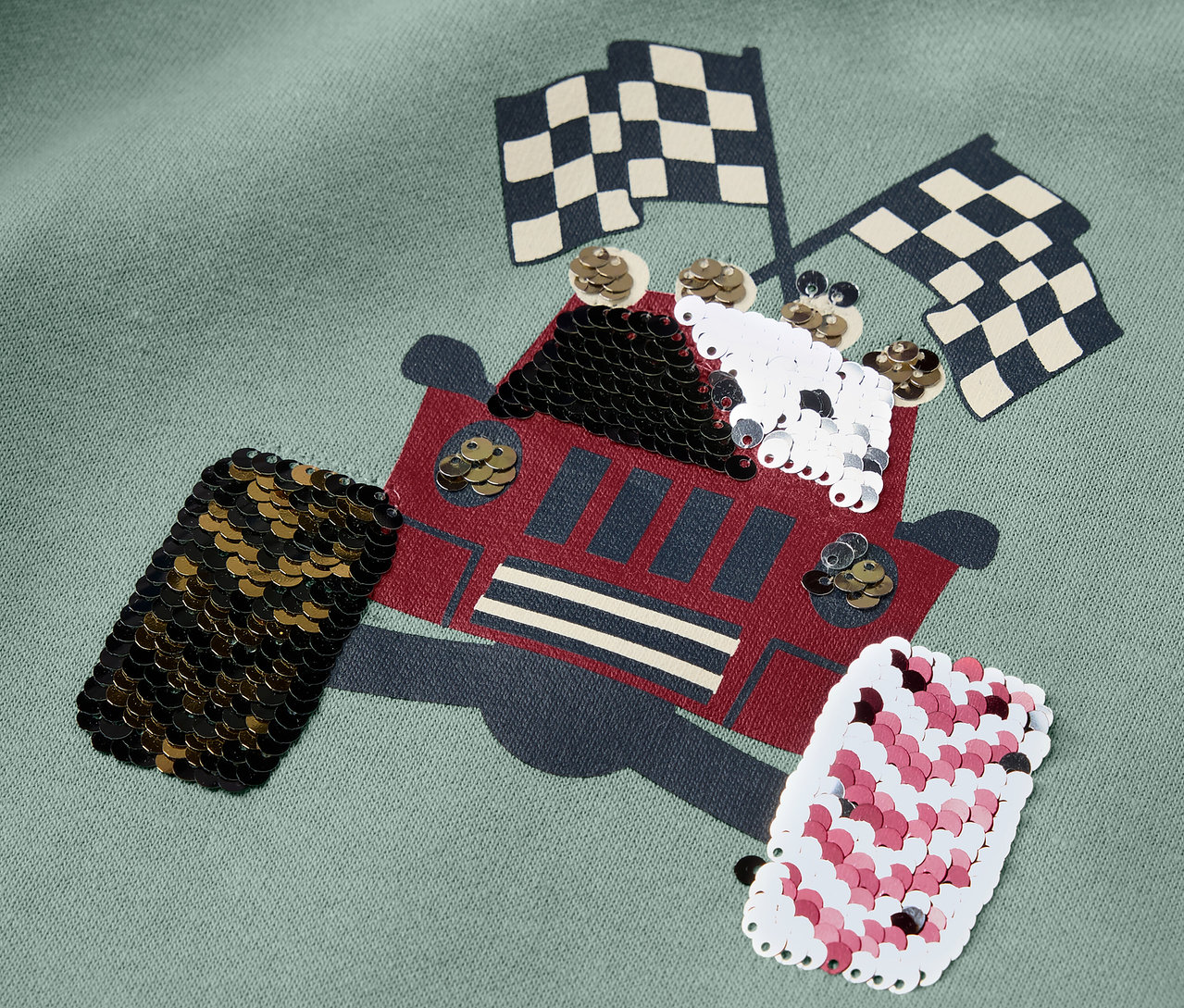 Detail dětské mikiny s aplikací náklaďáku a kostkovanými vlajkami.