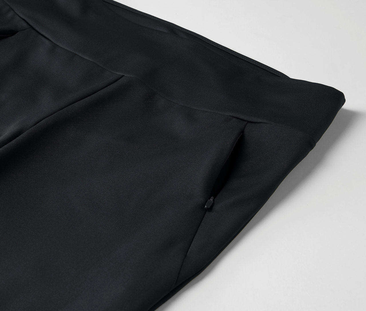 Detail černých kalhot s kapsou na zip.