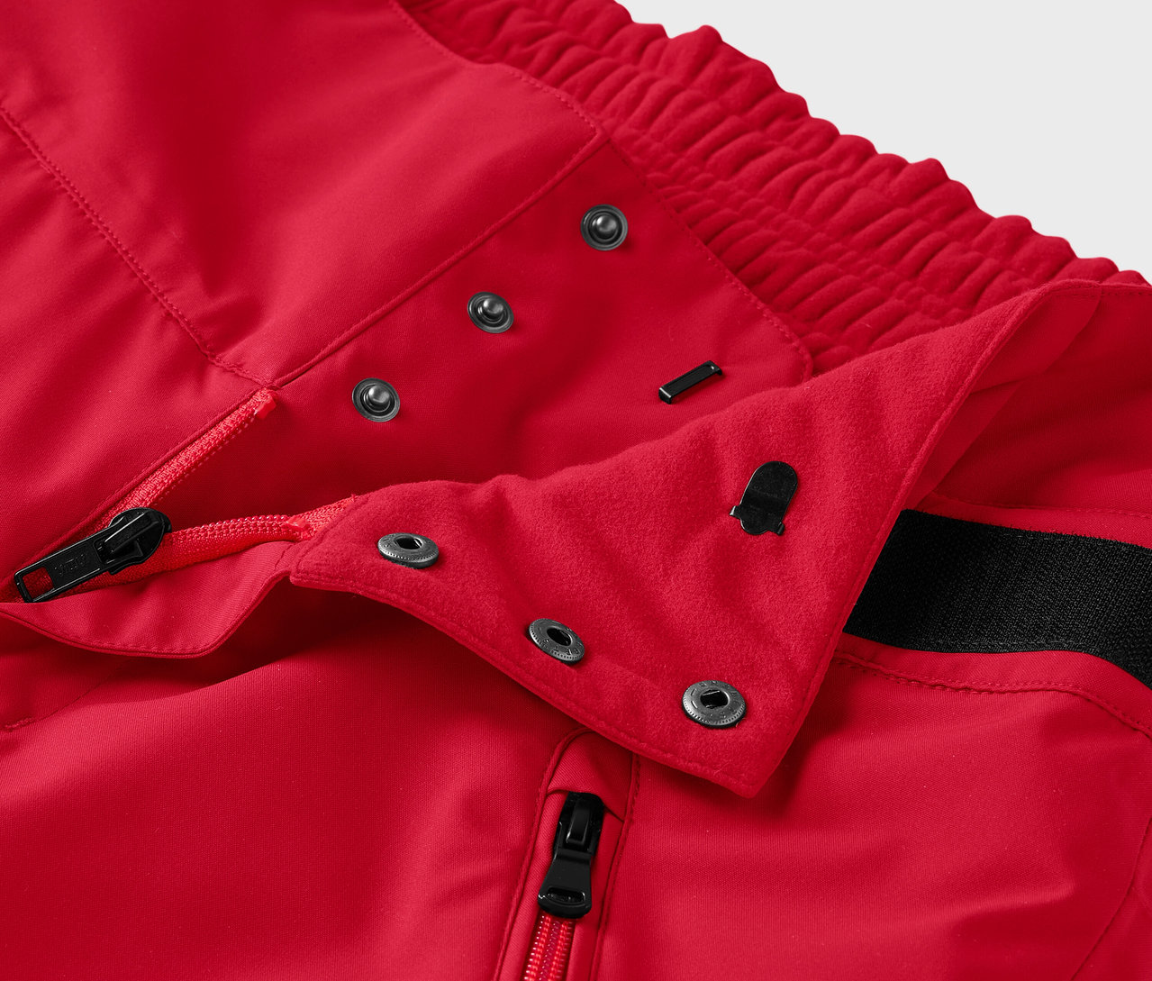 Detail červených kalhot se zipem a patentkami.