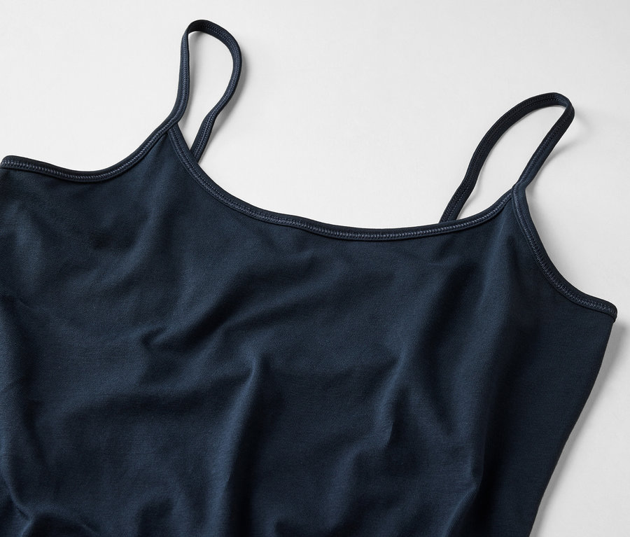 Detailní záběr na tmavě modré dámské tílko s tenkými ramínky na světlém pozadí.