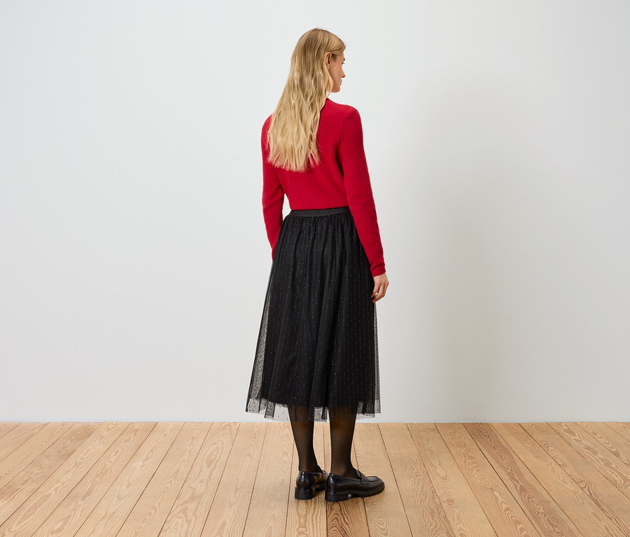 Žena zády k fotoaparátu má na sobě červený svetr a černou sukni.