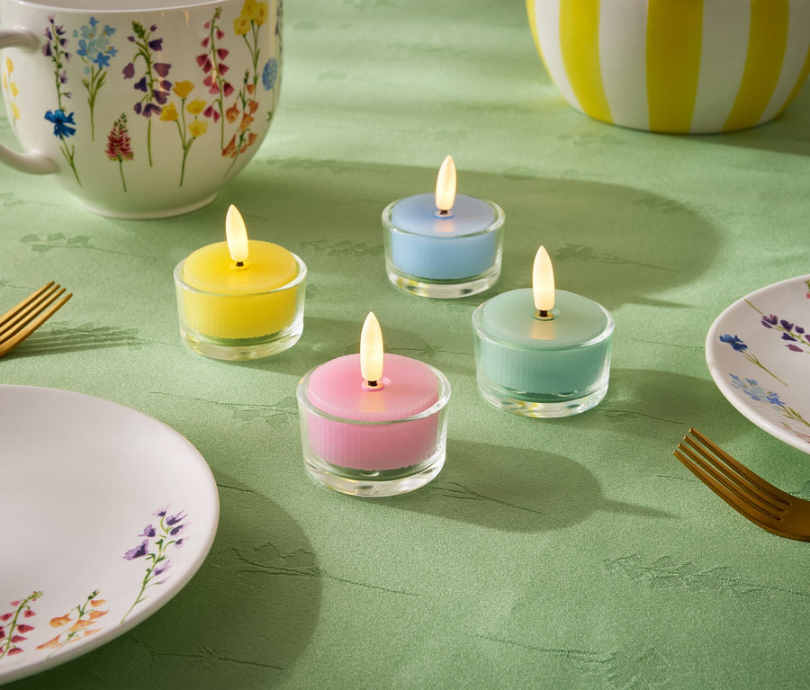 Na zeleném ubrusu jsou čtyři malé svíčky v pastelových barvách: žlutá, modrá, zelená a růžová. Dále je zde talíř, šálek a mísa s květinovým vzorem a dvě zlaté vidličky.