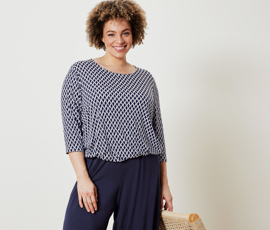 Žena pózuje v halence s potiskem a tmavě modrých kalhotách se širokými nohavicemi.