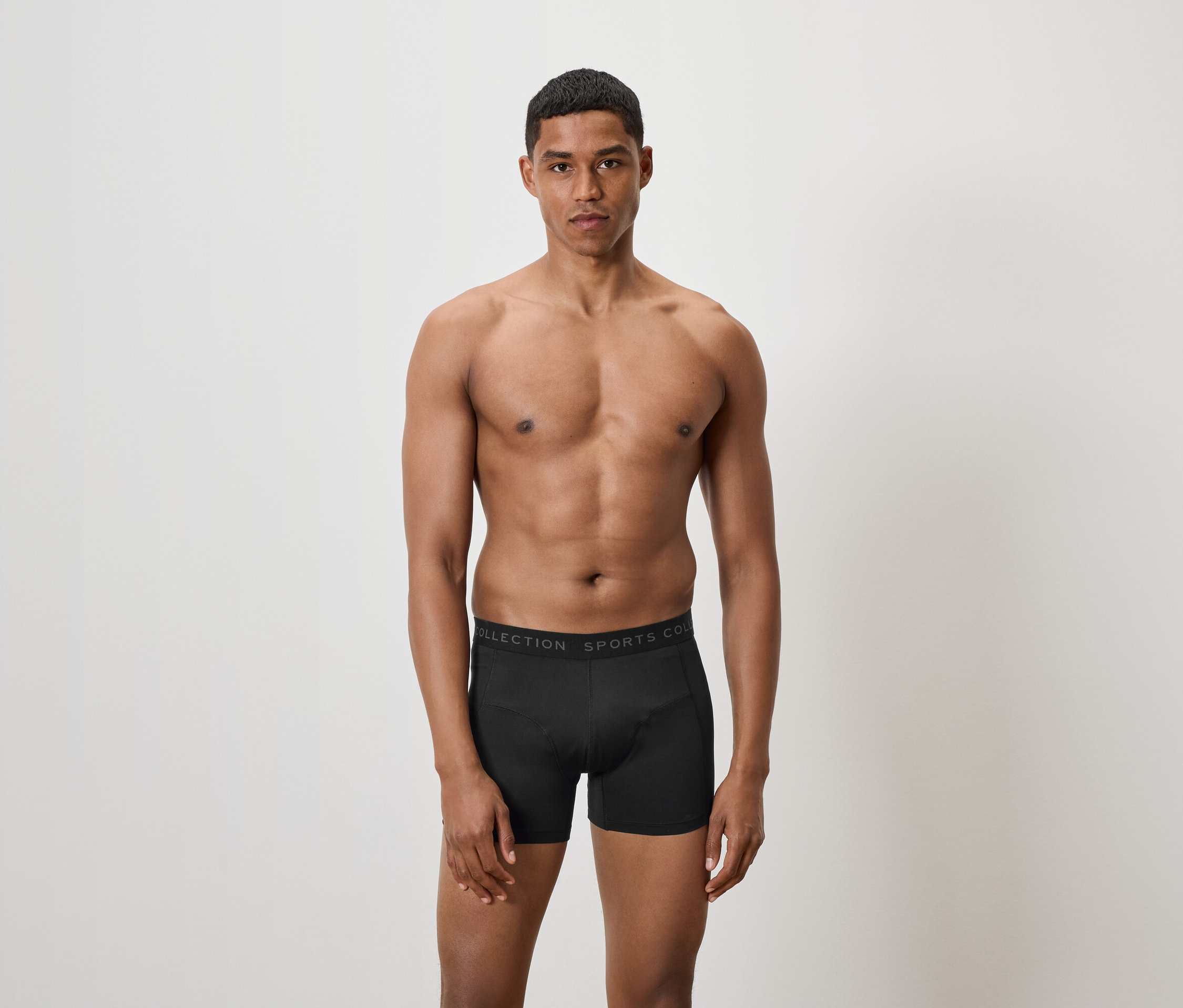 Muž bez trička pózuje v černých boxerkách.