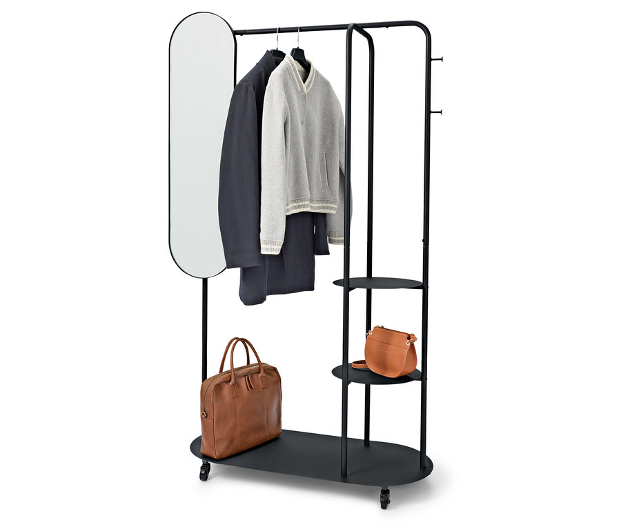Černý stojan na oblečení s oválným zrcadlem, kabátem, svetrem, kalhotami a dvěma hnědými taškami.