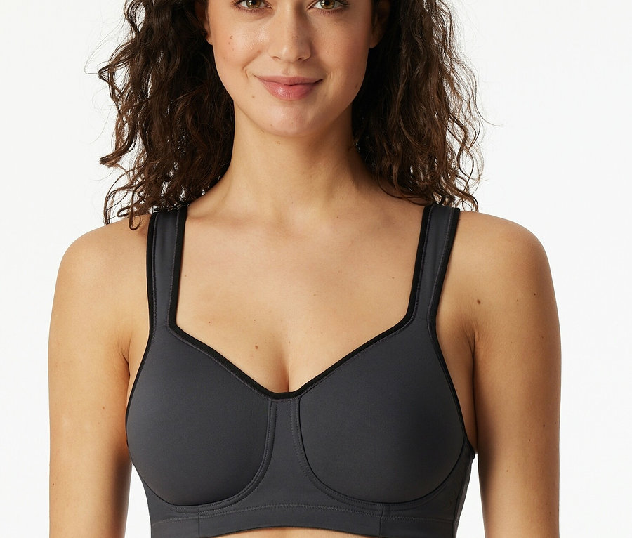 Usmívající se žena má na sobě šedou sportovní podprsenku.